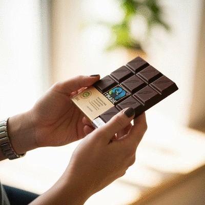 Hands holding a bar of vegan chocolate with a Fair Trade logo visible, symbolizing ethical consumption